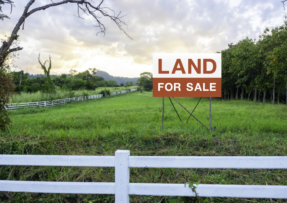 A land for sale sign in front of a white fence.